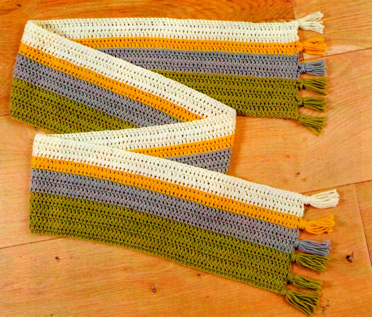 Bufanda de rayas a ganchillo para principiantes (patrón gratis) 2 Bufanda de rayas a ganchillo extendida sobre una mesa de madera, con flecos de colores